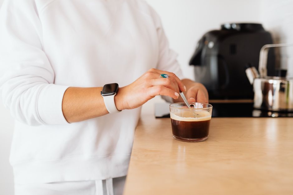 A person stirring coffee in a clear glass wearing a smartwatch, creating a cozy morning vi