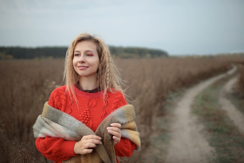 A woman in a red sweater embraces the outdoors in an autumn field, exuding warmth and joy.