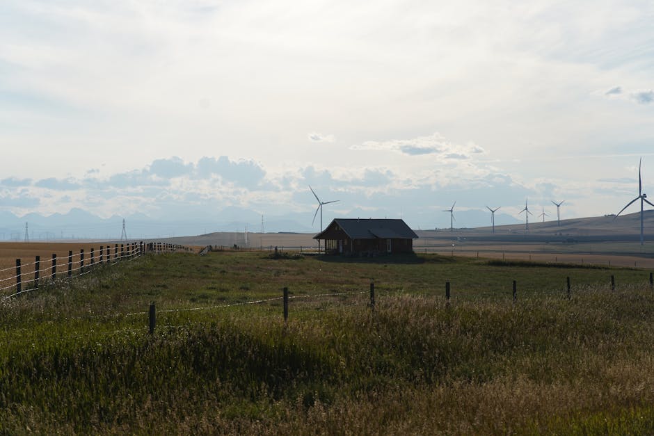 Scenic Canadian farm landscape showcasing a red farmhouse, wind turbines, and open fields under a cloudy sky.