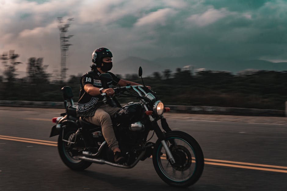 A motorcycle rider cruising down a deserted road at twilight with scenic mountain views.