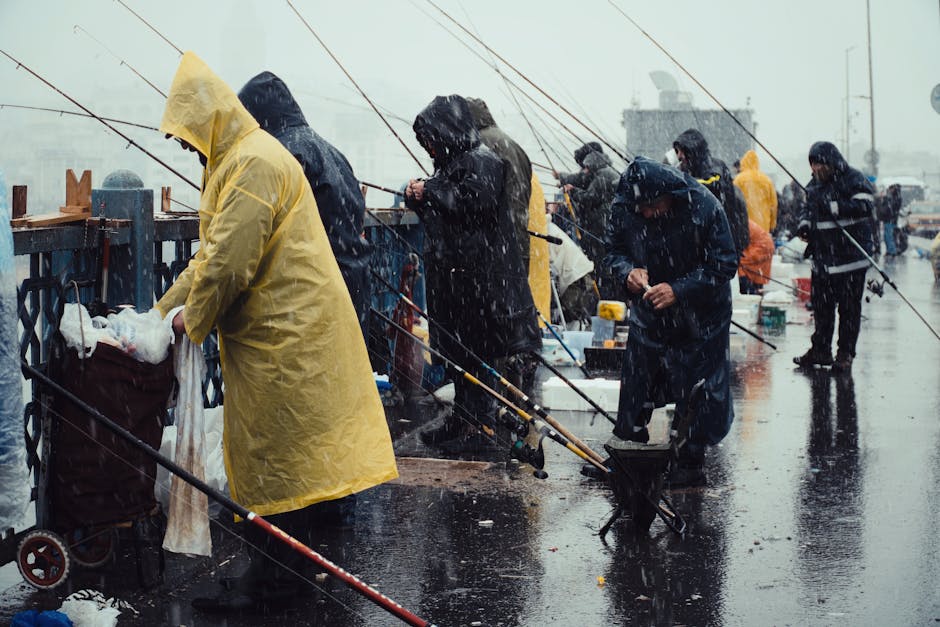 Group of people fishing on a rainy day, wearing yellow raincoats, urban setting.