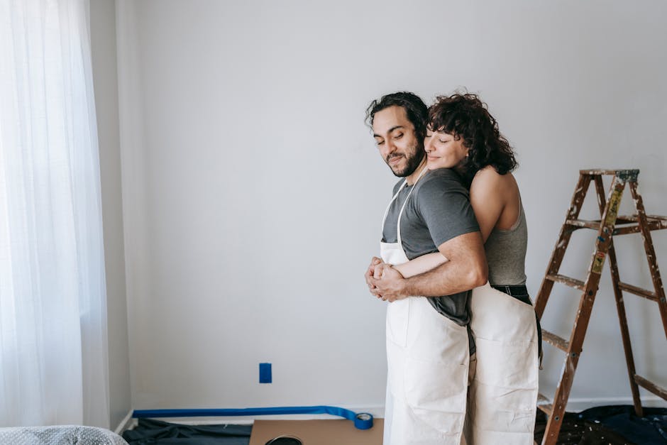 A couple lovingly embraces while renovating a room, conveying warmth and teamwork.