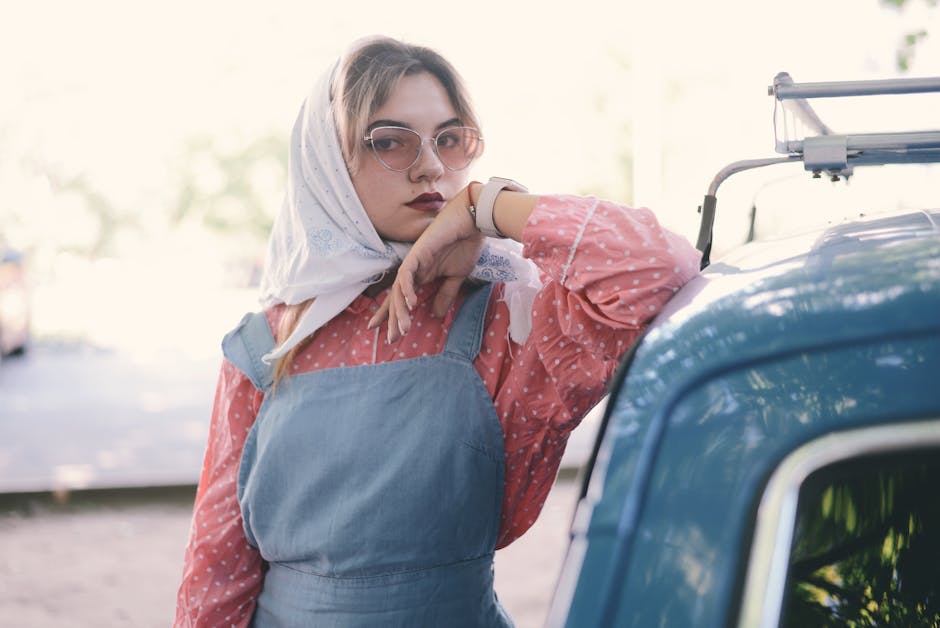 Young woman in stylish attire with sunglasses posing by a vintage car.