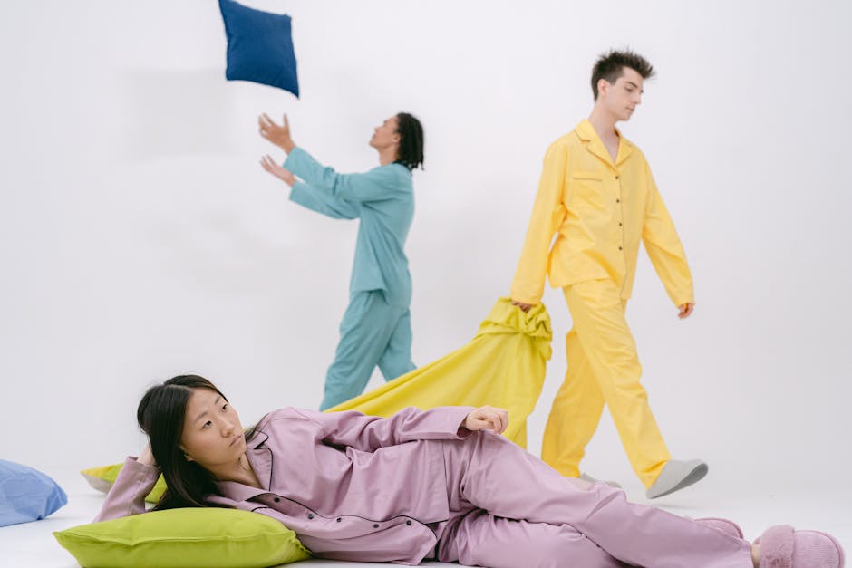 Young adults in colorful pajamas having fun in a room with pillows on a white background.