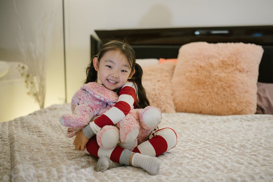 Happy child with stuffed toy, sitting on a bed, smiling in a cozy bedroom setting.