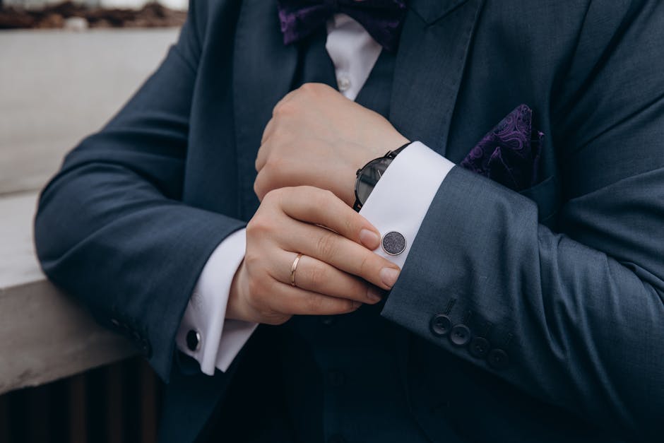 Close-up of a man adjusting his suit jacket cuff with a watch and ring visible, showing elegance.