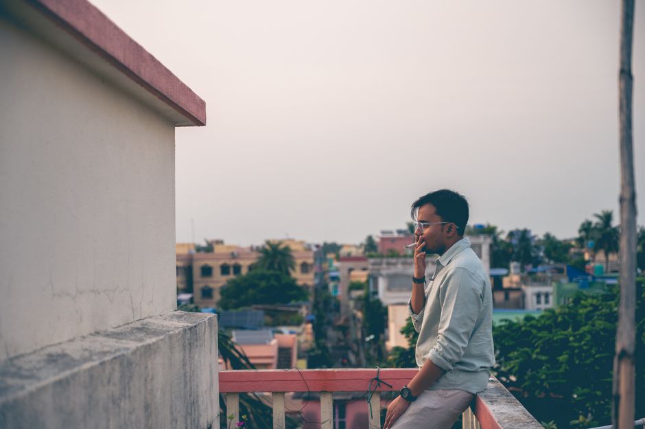 A man smoking on a rooftop, overlooking a cityscape, captures a contemplative moment at sunset.