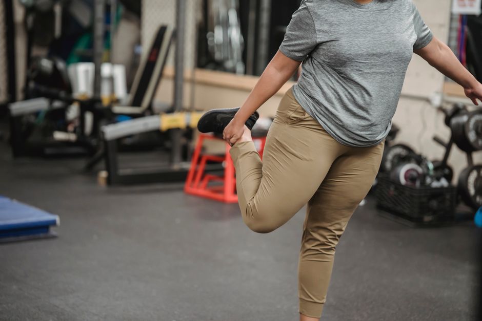 Crop anonymous female in sportswear stretching legs on blurred background of sport club with gym equipment