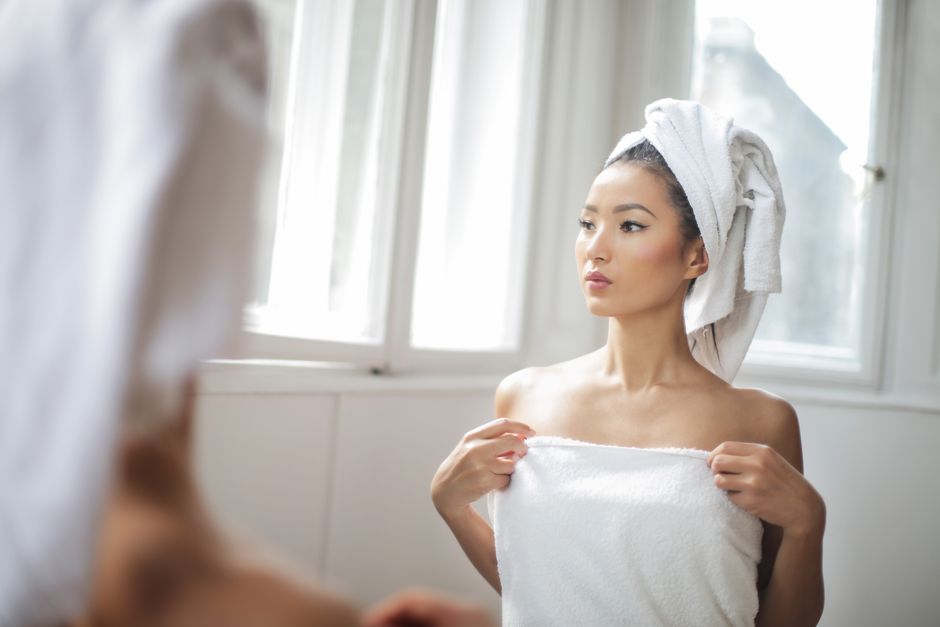 Portrait of an Asian woman wrapped in a towel, looking at her reflection in a bathroom mir