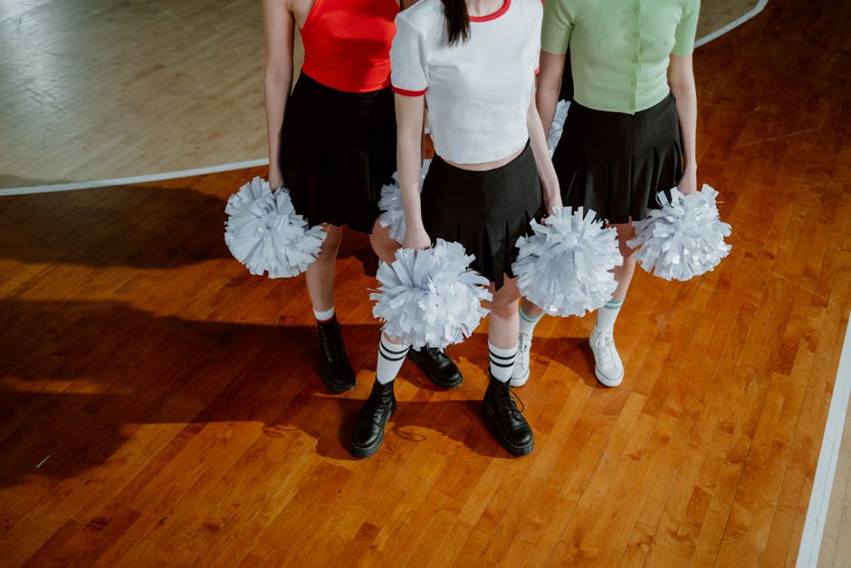 Three cheerleaders holding pom poms standing indoors on basketball court.