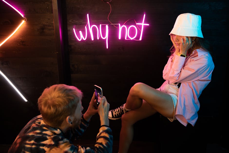 Two friends enjoying a neon-lit photoshoot, capturing fun moments indoors.