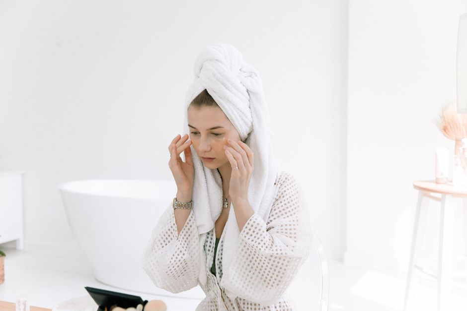 Woman in white bathrobe applying skincare in a bright bathroom. Perfect for wellness and b